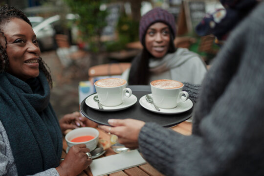 Waitress serving cappuccinos to mother and daughter at sidewalk cafe
