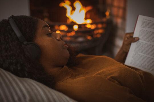 Serene woman with headphones reading book at fireplace