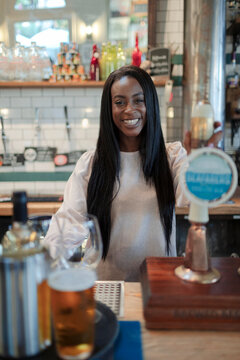 Portrait happy young female bartender working behind bar