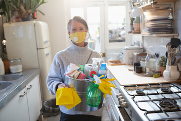 Portrait confident woman in face mask with kitchen cleaning supplies