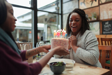 Happy mother and daughter celebrating birthday with cake in cafe