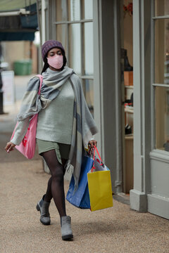 Young woman in face mask with shopping bags on sidewalk