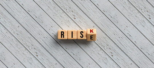 Risk versus Rise concept with revolving alphabet letters on wooden cubes over a diagonal grey wood plank background with copyspace in a panorama banner