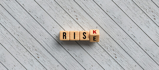Risk versus Rise concept with revolving alphabet letters on wooden cubes over a diagonal grey wood...
