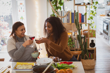 Mother and daughter cooking and drinking wine in kitchen