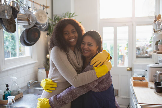 Portrait happy mother and daughter in rubber gloves hugging in kitchen