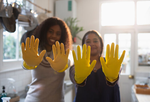 Portrait playful mother and daughter gesturing in yellow rubber gloves