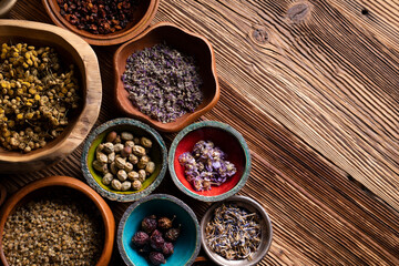 Natural medicine background. Assorted dry herbs in bowls and brass mortar on rustic wooden table.