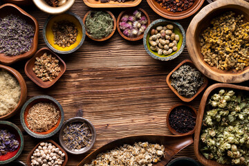 Natural medicine background. Assorted dry herbs in bowls and brass mortar on rustic wooden table.