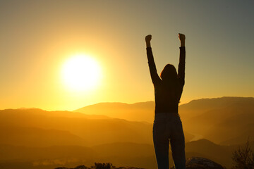 Silhouette of a woman celebrating raising arms at sunset