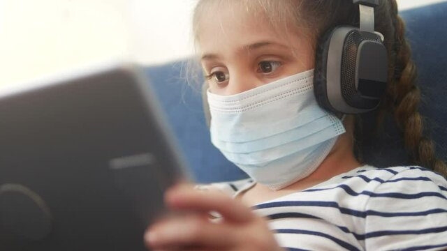 distance learning online lessons. child girl with digital tablet in mask studying remotely at home. education coronavirus online lessons lockdown concept. child learns distance learning online