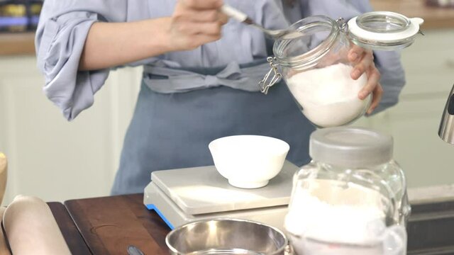 A girl's hand up Scooping sugar out of the jar To weigh in the preparation of ingredients for baking