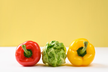 Fresh cos lettuce and bell peppers in on white and yellow background