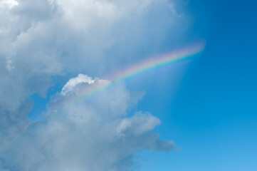 A soft rainbow formed in the clouds with a blue sky in the background. Iriomote Island.