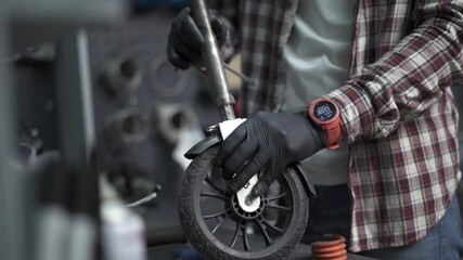 Professional craftsman working on electric scooter in workshop. Technicians fixing wheel from kids push scooter in repair shop. Mechanic at work. Eco-friendly transport. Scooter maintenance service