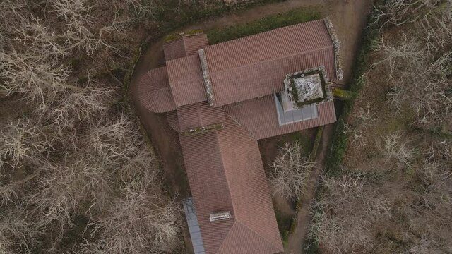 Plano a&eacute;reo en zenital (overhead) zona zoom out de in monasterio rodeado de &aacute;rboles sin olas en invierno, al atardecer