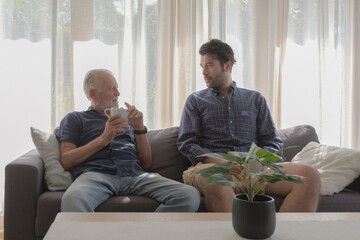 Two old father and son family relax talking and drinking coffees at sofa living room warmth house...