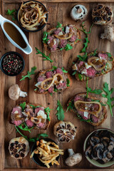 Top down close up view of open faced steak sandwiches on a wooden platter surrounded by toppings.