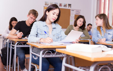 Fototapeta premium Smiling schoolgirl is learning and answering the question on paper in the class.