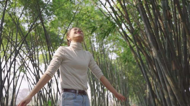 4k slow motion of Young beautiful Chinese girl enjoys the spring sunshine Young Asian women smiling and looking up smile in the bamboo forest Healthy lifestyle concept people love the nature