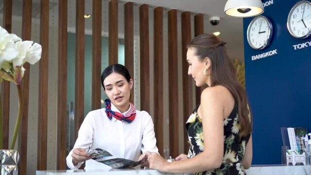Tourist comes to the reception in the hotel and gives her passport. Receptionist politely checks her passport and gives her the form to fill,  Business, travel and people concept