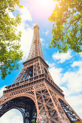 Eiffel Tower against the sky with green trees in Paris, France. Famous travel destination. - obrazy, fototapety, plakaty