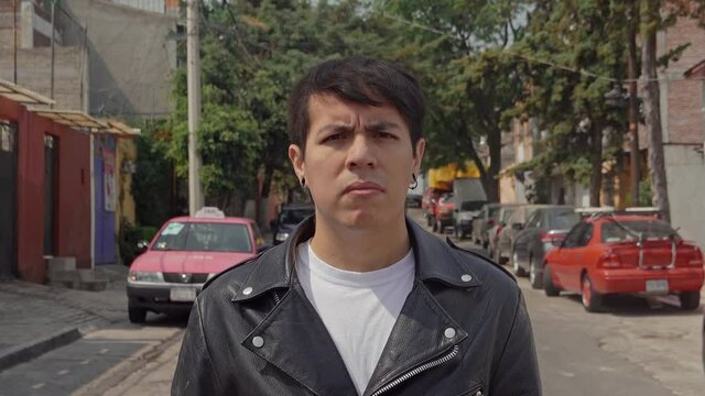 Portrait of a latino young male punk rocker adult staring at the camera with a a serious expression and a leather jacket on 