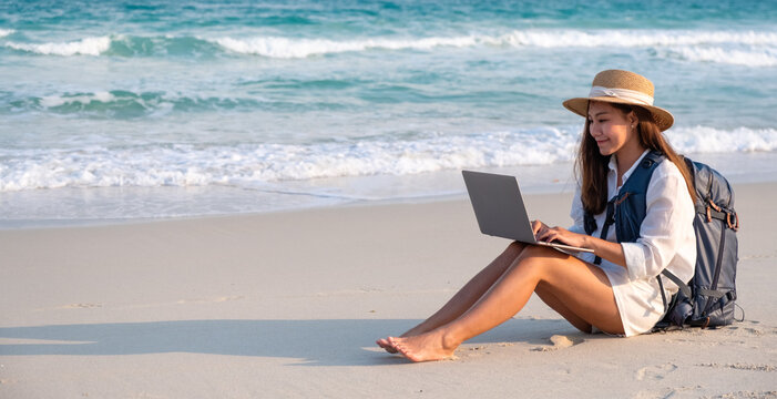 A female traveler using and working on laptop computer while sitting on the beach