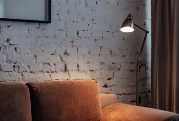 Golden floor lamp and orange comfortable sofa in an elegant living room interior with an old brick wall
