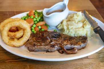Delicious grilled beef steak with onion rings , vegetable , mashed potato and red wine sauce and vegetable on white plate in Scotland