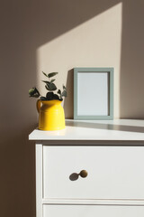 Yellow ceramic jug or vase with eucalyptus branches, empty white photo frames