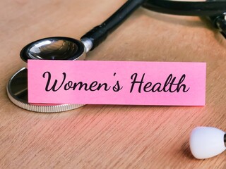 Phrase WOMEN'S HEALTH written on pink sticky note with stethoscope. Medical and health concept.