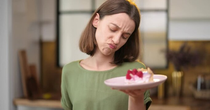 Young thoughtful woman makes a choice between healthy food and sweet dessert, having a snack on the kitchen at home