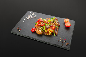 Chicken fillet in sweet and sour sauce with vegetables. On a black slate board. Dark background. Isolated