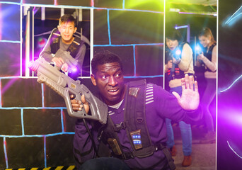Portrait of happy positive African-American with laser gun having fun on dark laser tag arena