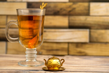 Vintage tea strainer and a glass of tea on a wooden table with place for text. Teapot-shaped golden tea strainer