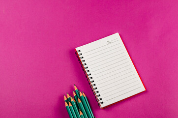 Open spring-loaded notebook and pencils on a pink background.