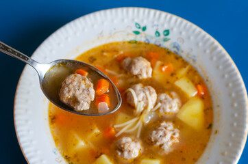 A spoonful of soup with meatballs on the background of a white c