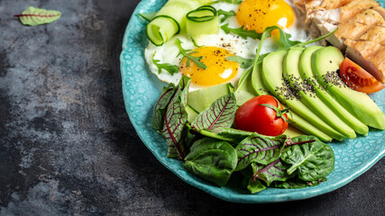 Tasty breakfast with fried eggs with cherry tomatoes , avocado, chicken grilled fillet, cucumbers, and avocado. Healthy breakfast. top view