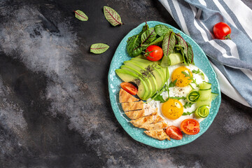 Plate with a keto diet food. Fried egg, cherry tomatoes , avocado, chicken grilled fillet, cucumbers, and avocado. Healthy breakfast. top view