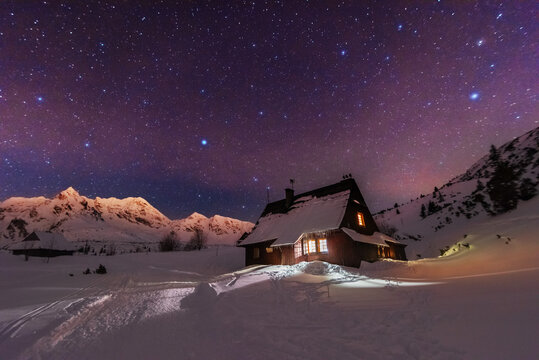 Night winter landscapes in the High Tatras, with mountain houses on a background of snow-capped mountains and starry sky