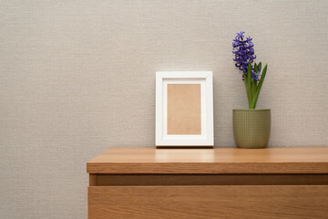 Wooden chest of drawers with a white photo frame next to a blooming blue hyacinth.