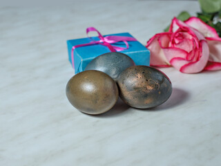 Painted for Easter egg, box with gift and bouquet of roses lie on gray table