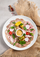 Cold Cut Meat Platter. Rustic style meat appetizers with dip and vegetables. Snack plate on grey table with sack napkin.