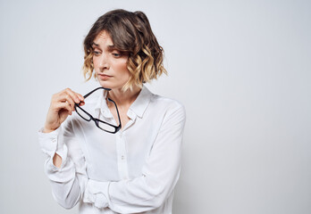 A beautiful woman in a white shirt holds glasses in her hands on a light background