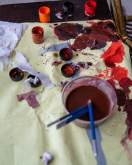 High angle view at artists palettes splattered with paint lying on table lit by sunlight, minimal...