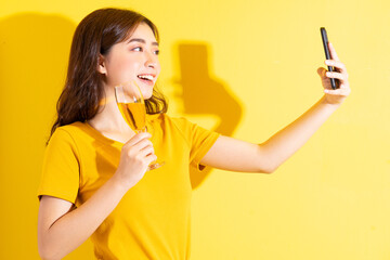Young Asian woman drinking wine and posing on yellow background