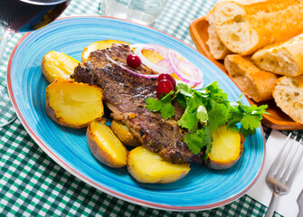 Tasty beef steak with baked potatoes served at plate with greens