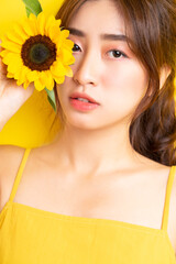 Beautiful Asian woman holding and posing with sunflower on yellow background