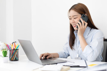 Asian female employee talking on the phone and working in a laptop with a smiling face, Office staff work and telephone conversations, Business conversation over the phone.